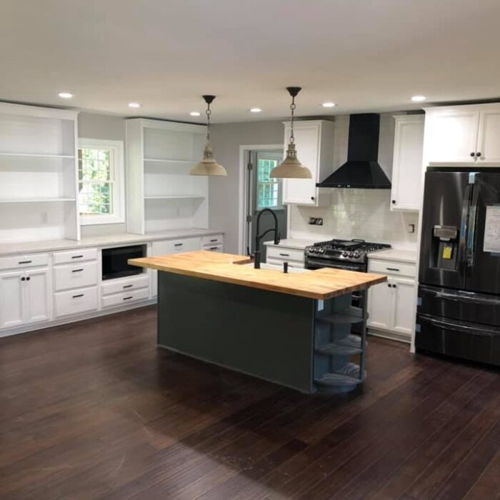 A bright kitchen remodel with a large gray island surrounded by white cabinets with white quartz countertops and butcher block countertops.
